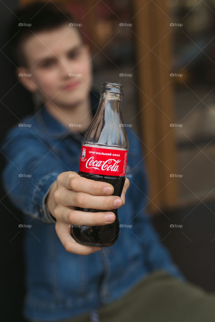 a guy in a denim jacket drinking Coca-Cola on the street.  handsome young man, teenager.  lifestyle photos