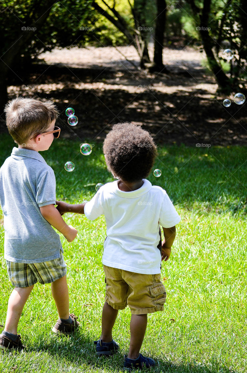 Two preschool boys playing with bubbles together outdoors on a bright summer day