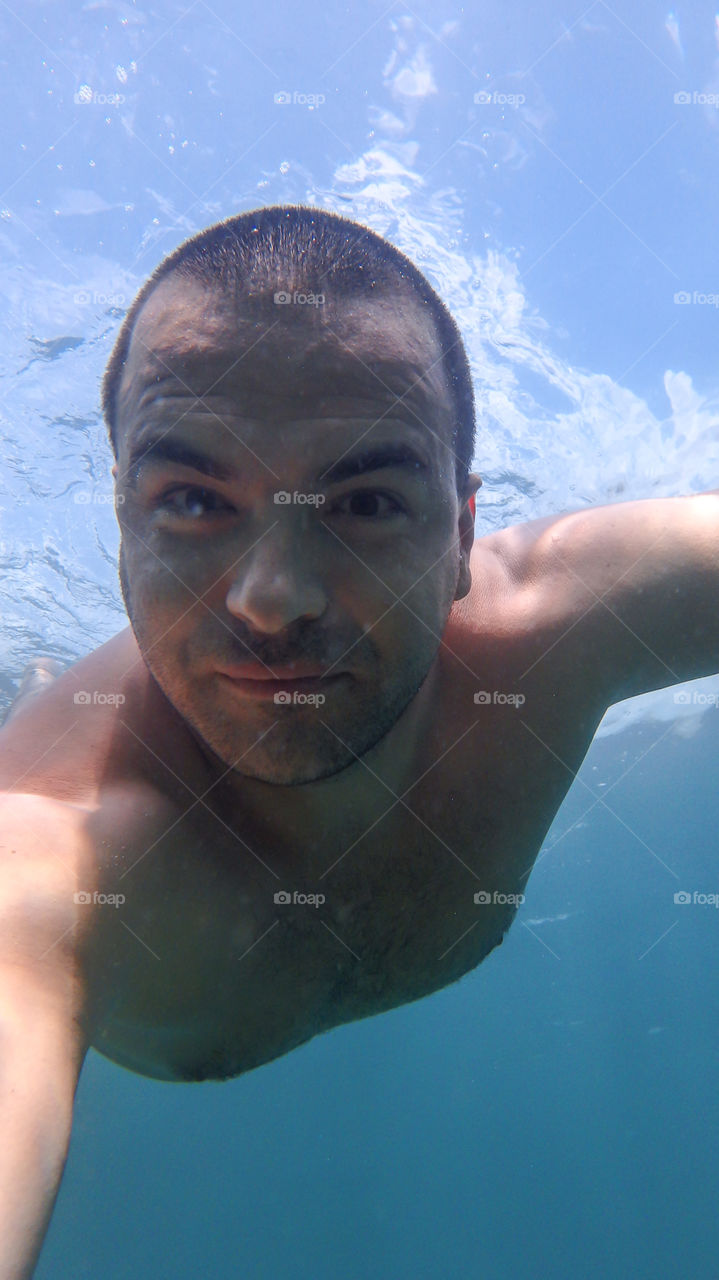 Man diving, man underwater smiling and relaxing in big blue sea