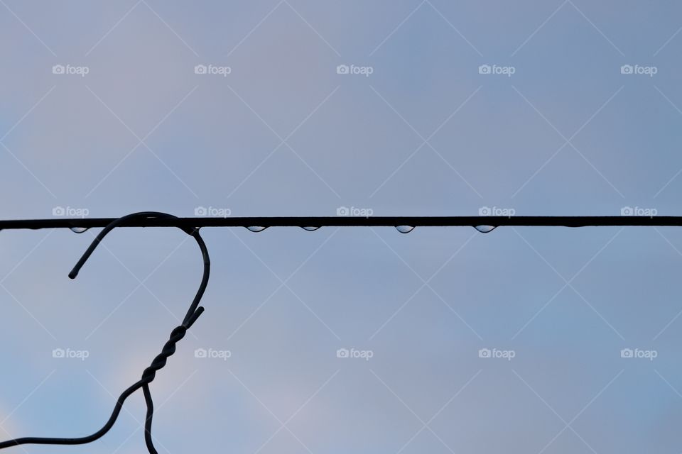 Wire coat hanger silhouette on metal outdoor laundry line at dusk after a rainfall