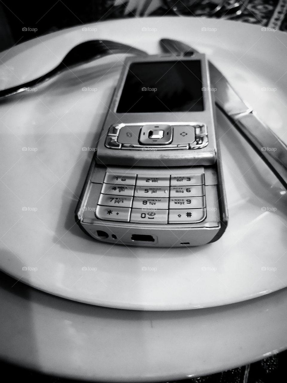 White plate served with a fork and a knife, on which lies the Nokia N95 phone