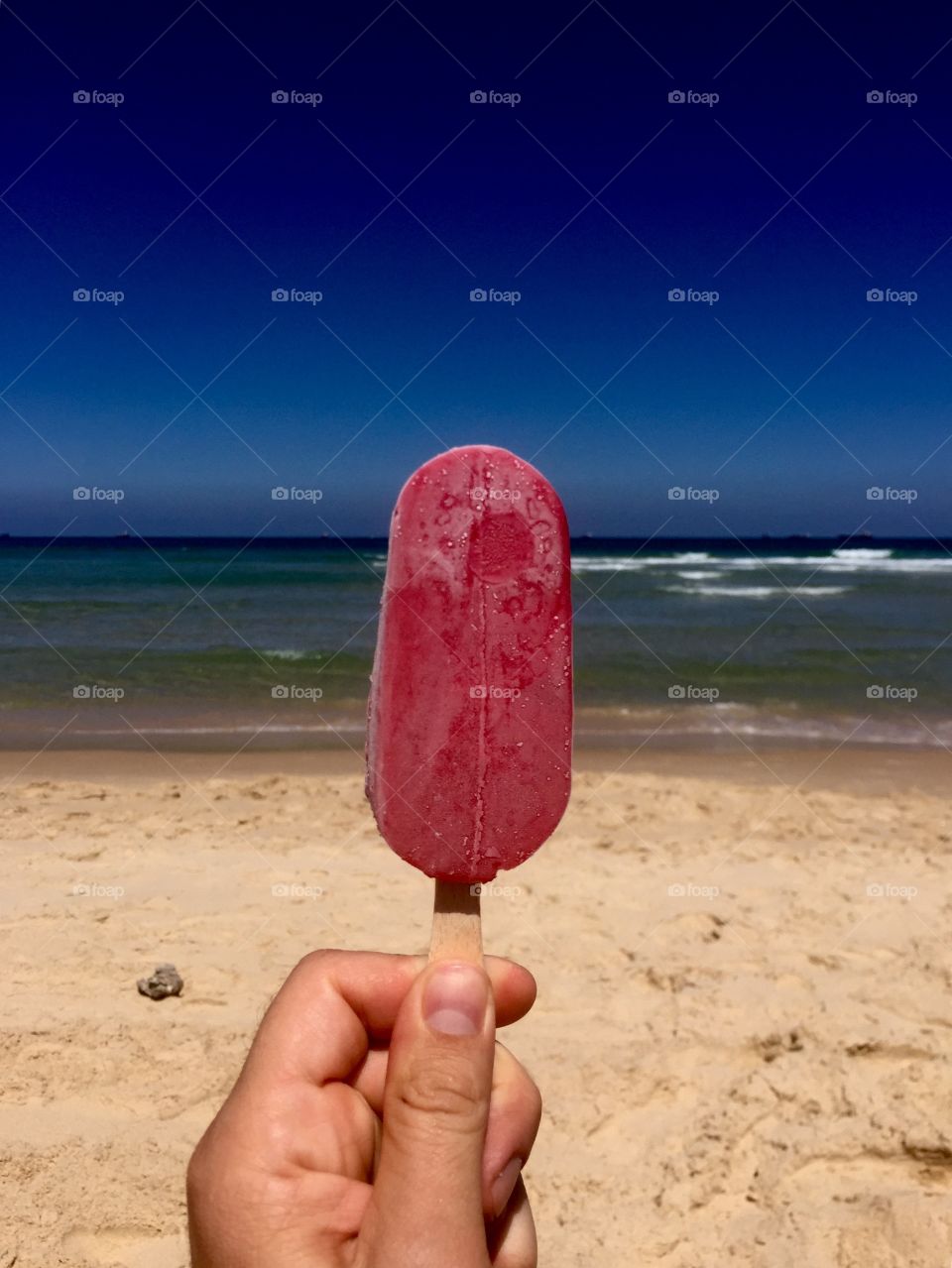 A person holding popsicle in front of beach