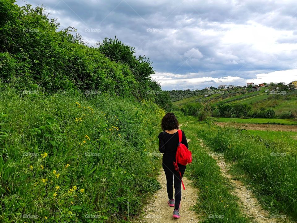 woman from behind walks alone in the countryside to respect social distancing