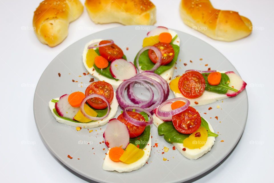 Mozzarella slices with carrots, spinach, onions and cherry tomatoes on a gray plate.  Angle view of food