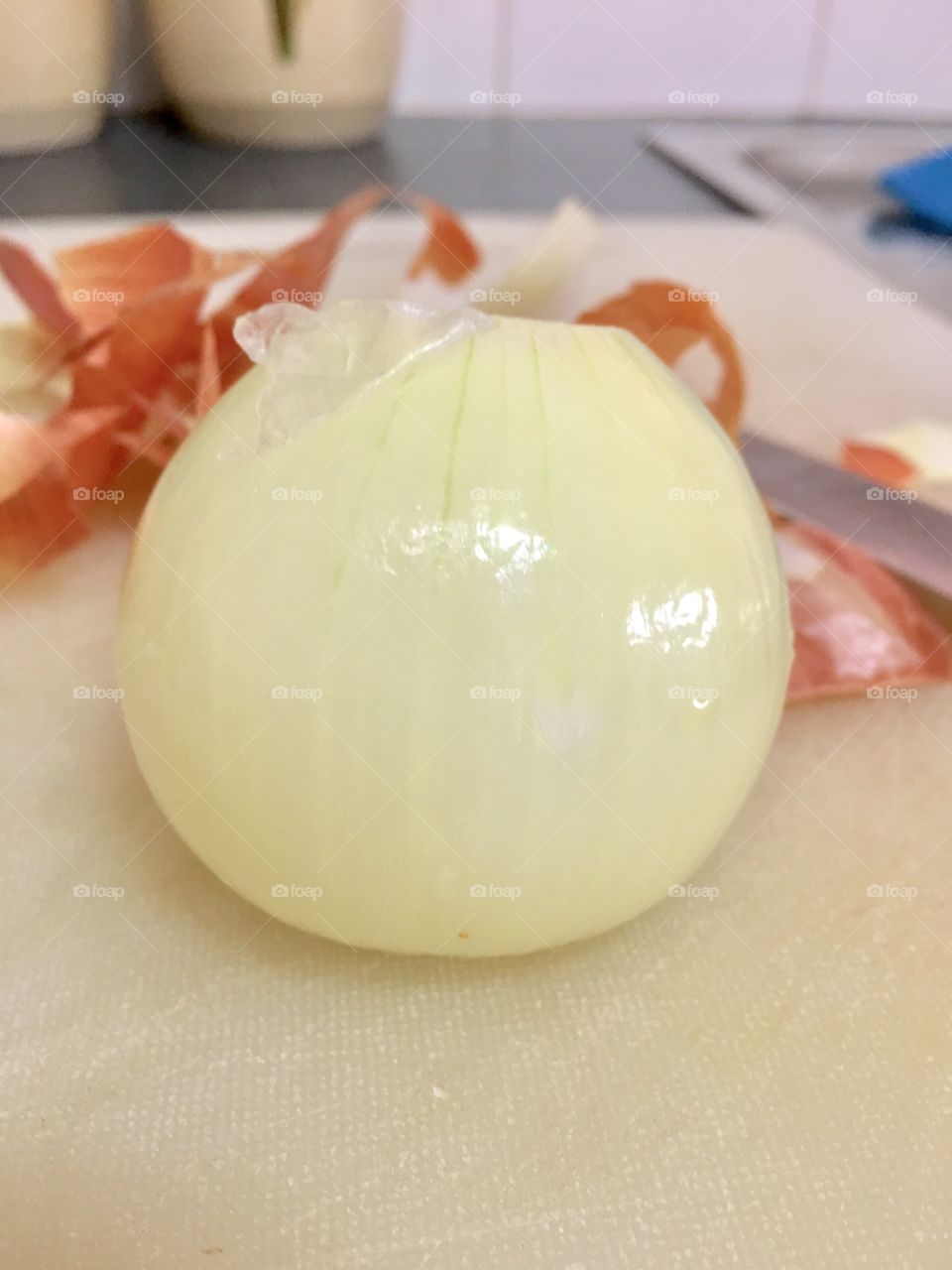 One white peeled onion foreground on cutting board, peelings blurred in background