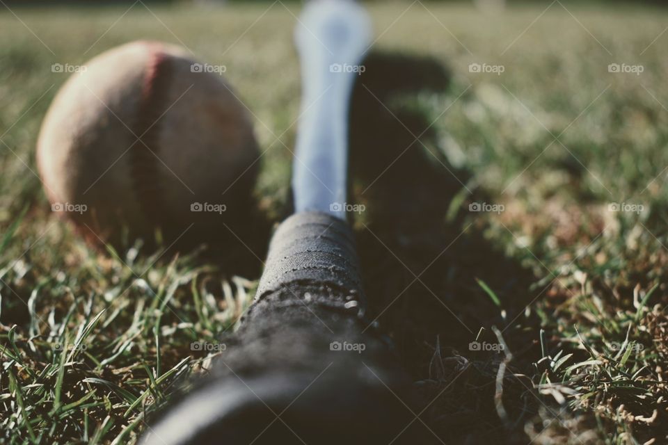 Full detail of a black baseball bat lying next to a baseball in short, freshly cut grass.