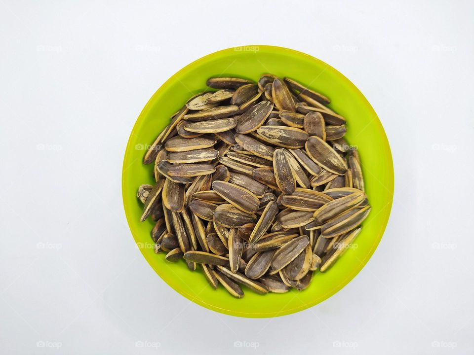 Sunflower seeds in green bowl isolated on white background.