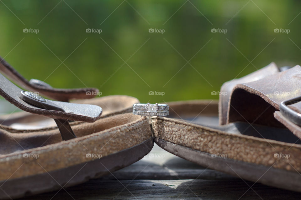 A wedding and engagement ring sit on top of men's and women's sandals on a dock