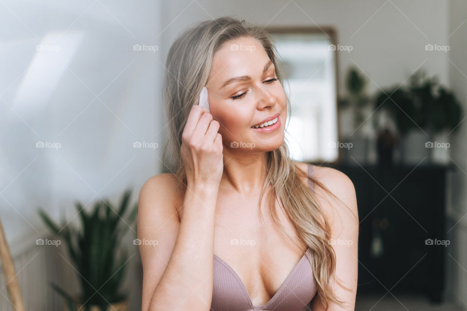 Young girl woman with guasha stone massager in hands in bath room spa beauty salon at home 