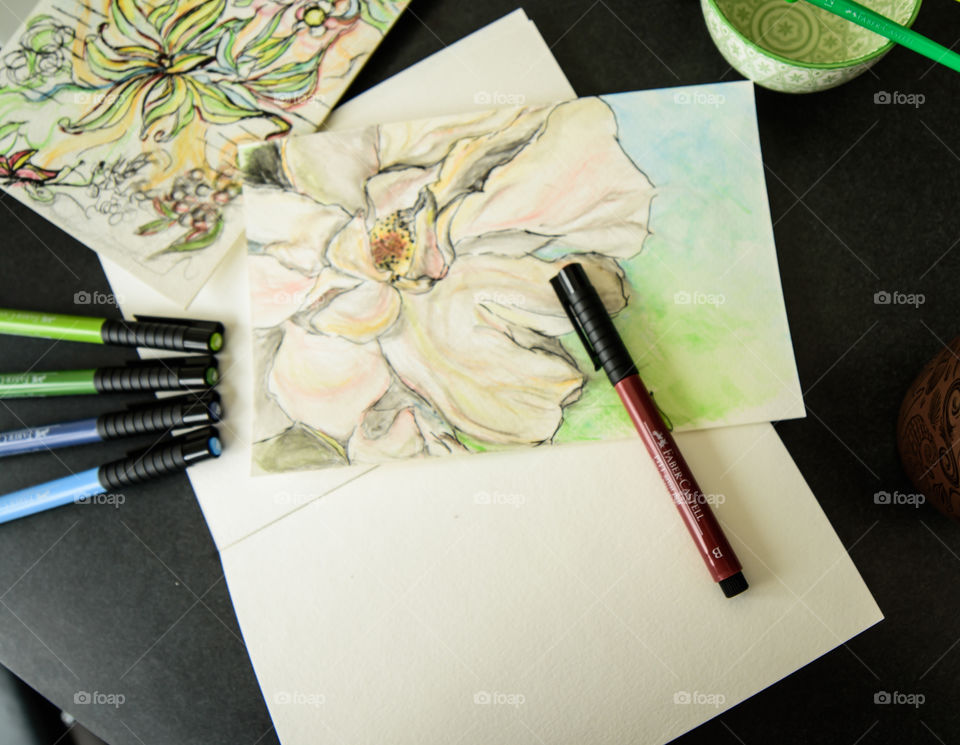 Faber-Castell PITT artist pens on desk with watercolor style painting sketch using Faber-Castell pens high angle view of spring flowers on sketch books 