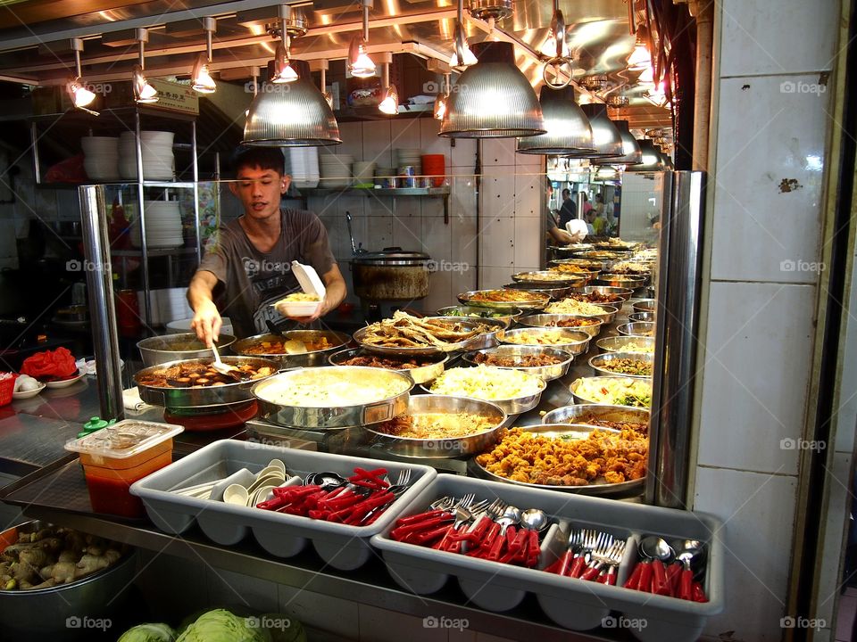 a man selling a variety of cooked food at a hawker