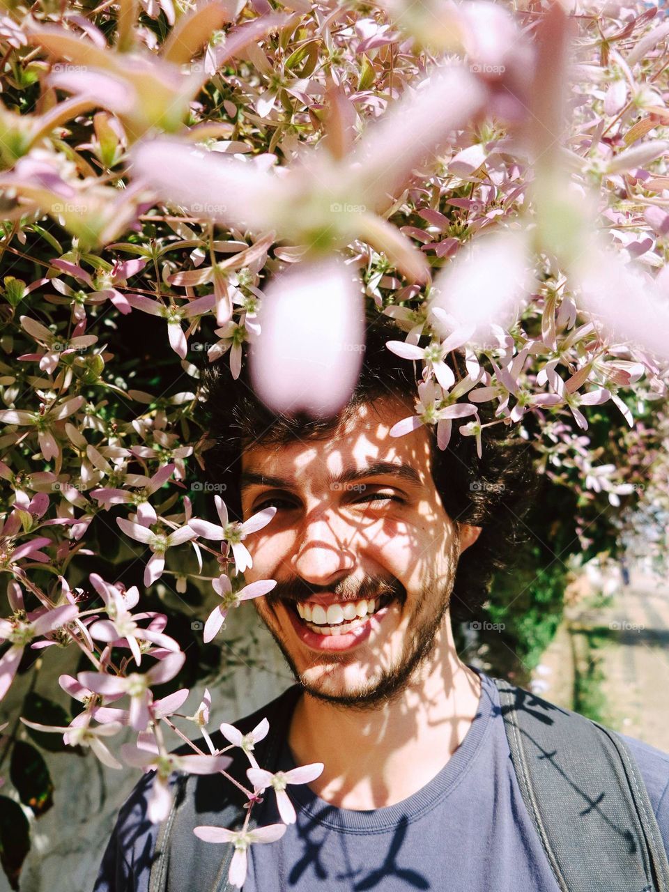 handsome man smiling, with pink flowers on the foreground and the background.