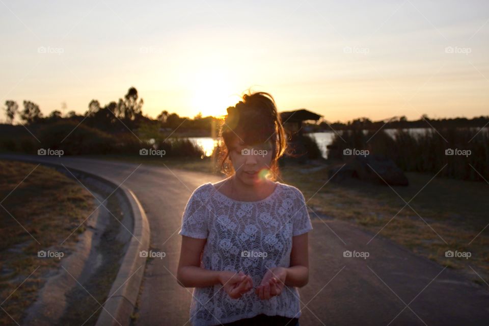 Ethereal sunset backlit photo of a young woman walking along a path wearing a white lace shirt