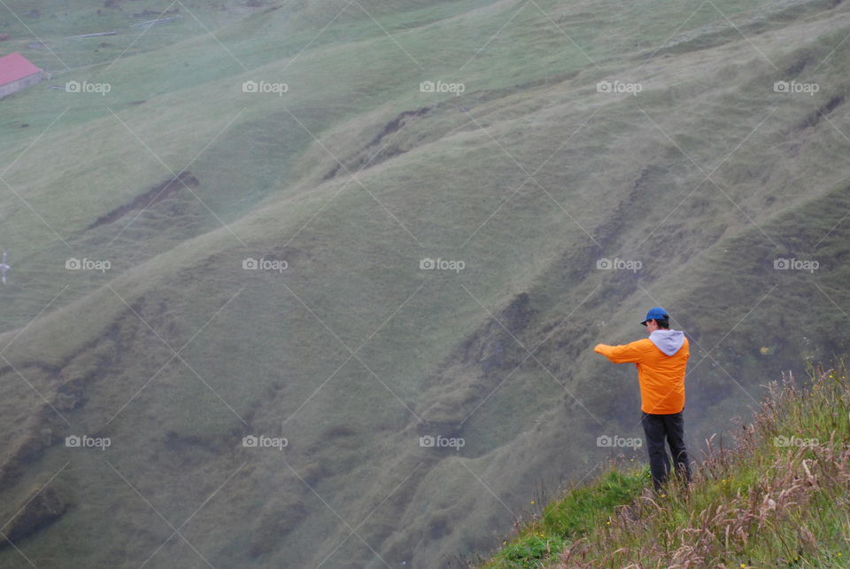 A man takes a picture over the edge of a precipice.