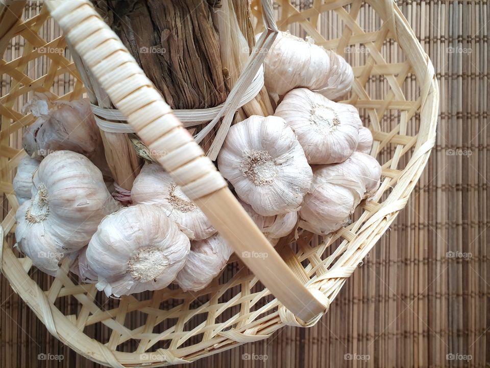 A bundle of organic Thai garlic the most widely used ingredients in Thai cuisine in a handmade basket on a bamboo mat - Top view closeup