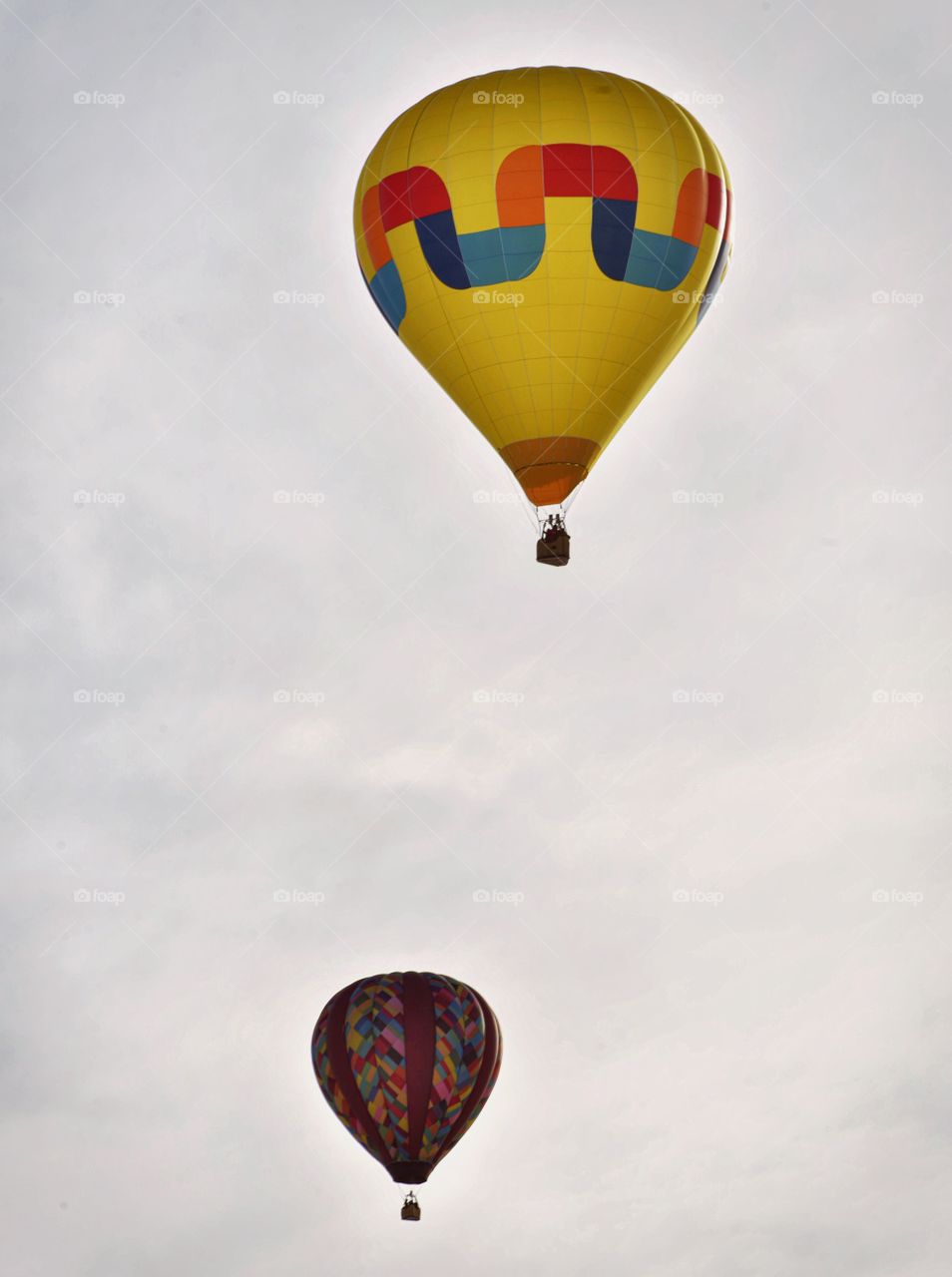 A hot air balloon festival in the winter creates a colorful scene. Clouds and sun create an atmospheric shot.