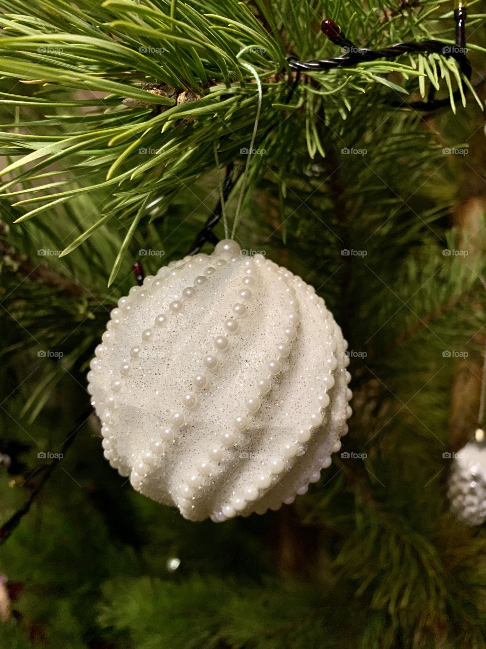 White Christmas ball decorated with beads hanging on a Christmas tree branch