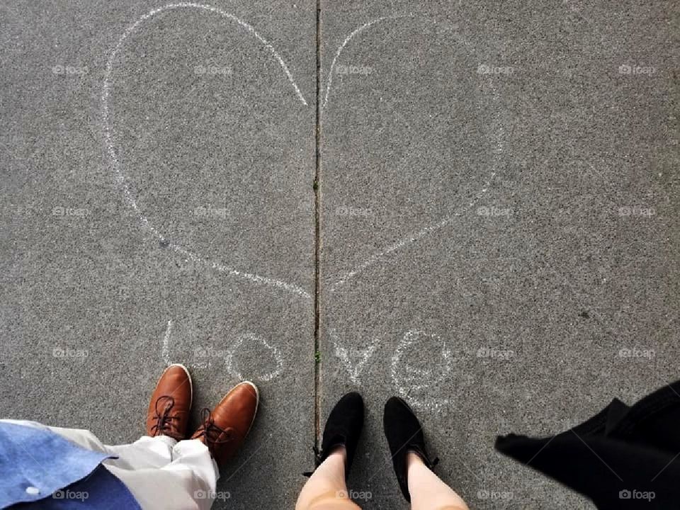 The word 'Love' written in sidewalk chalk. A couple stands, looking down.