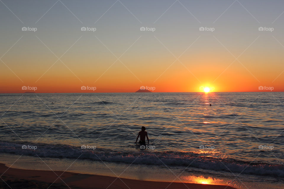 Silhouette of man in sea with dramatic sky at sunset