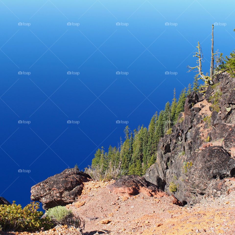 The rugged rim around the stunning rich blue waters of Crater Lake in Southern Oregon on beautiful sunny summer morning. 