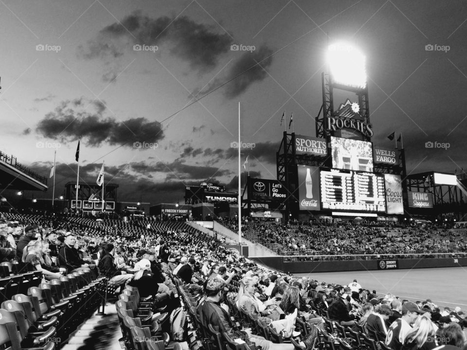 Scoreboard . Black and white evening shot of people and scoreboard at Coors Field.