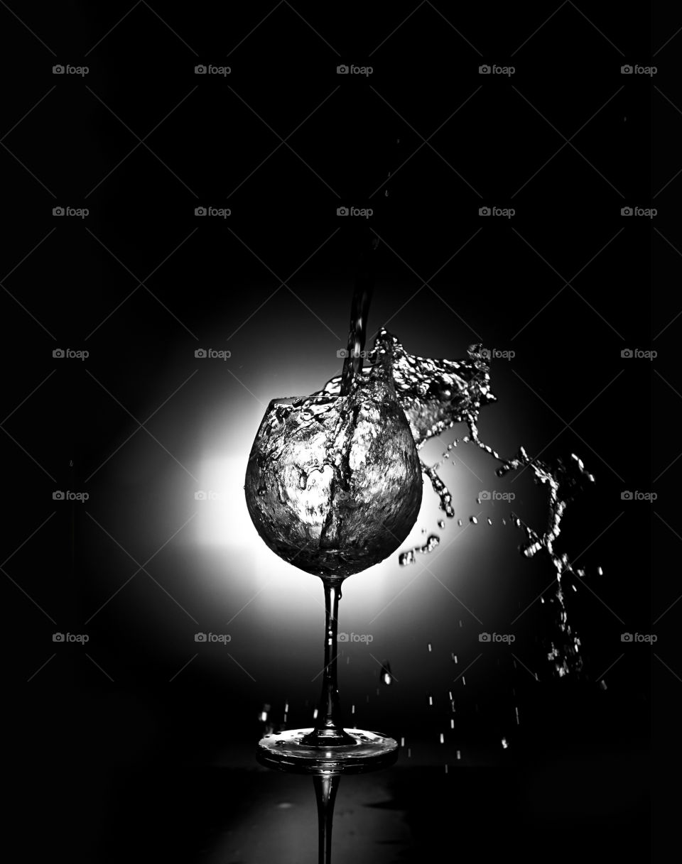 Clean water splashing in a glass of wine, black background with flash light on the back. Studio shot.