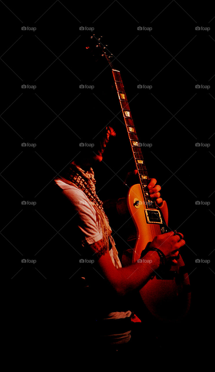 A guitarist posing in the spotlight holding up his guitar during a solo. Shot against a black background. 