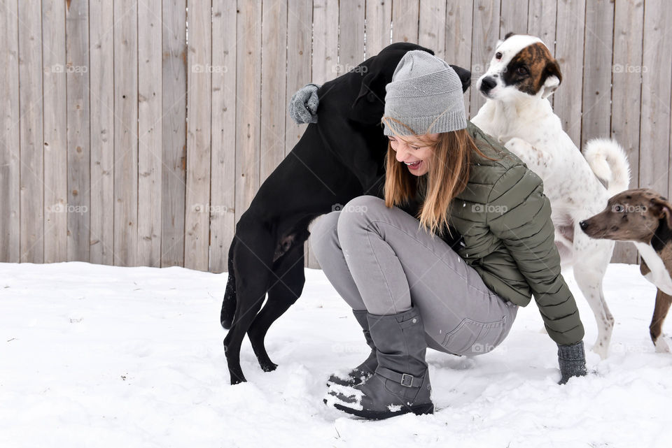 Millennial woman laughing and playing with her dogs in the snow