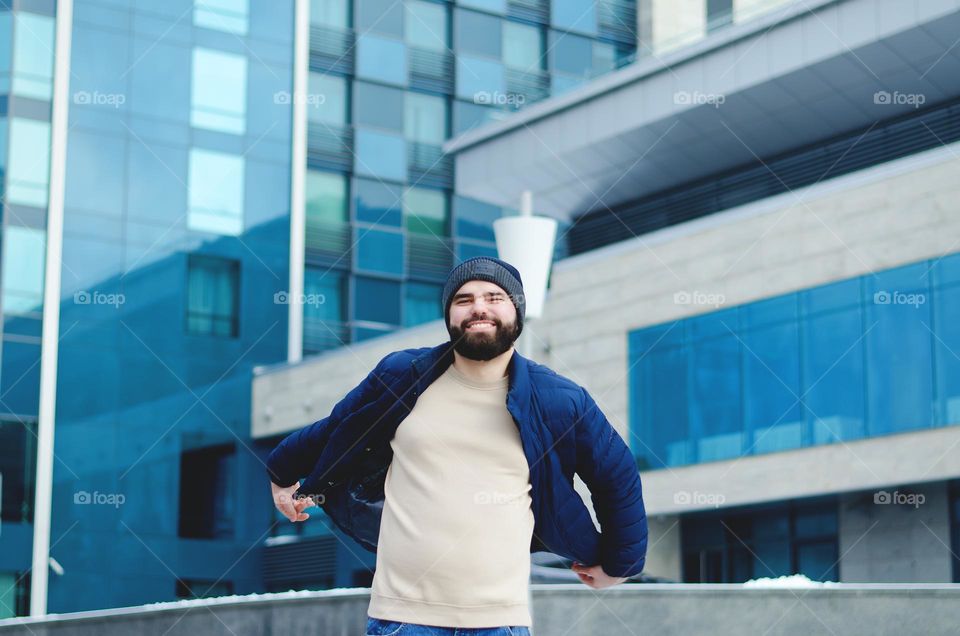 Portrait of happy, smiling, friendly bearded young man in casual clothes walking in city street in winter. Ukraine