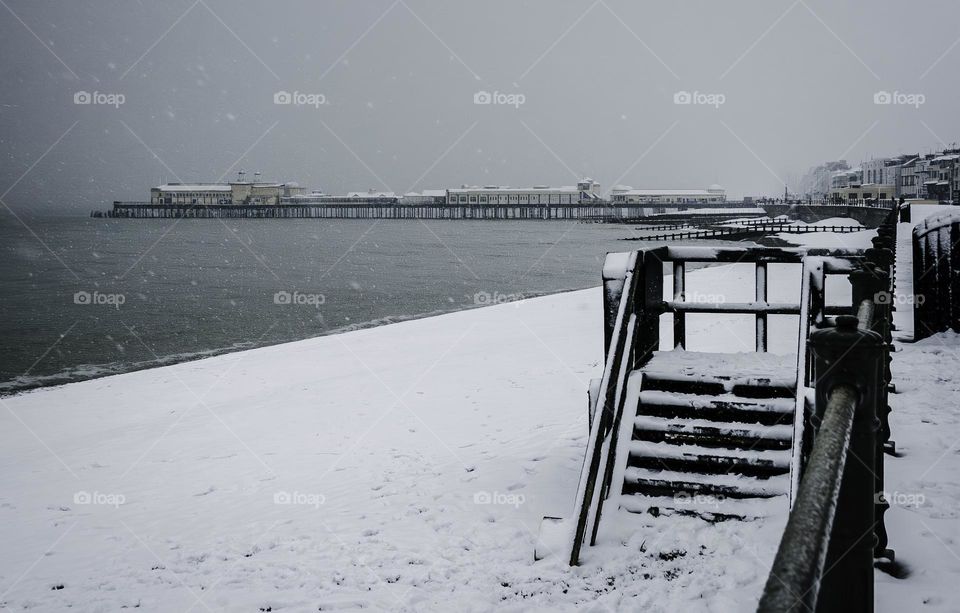 Snow covered beach with pier in the distance