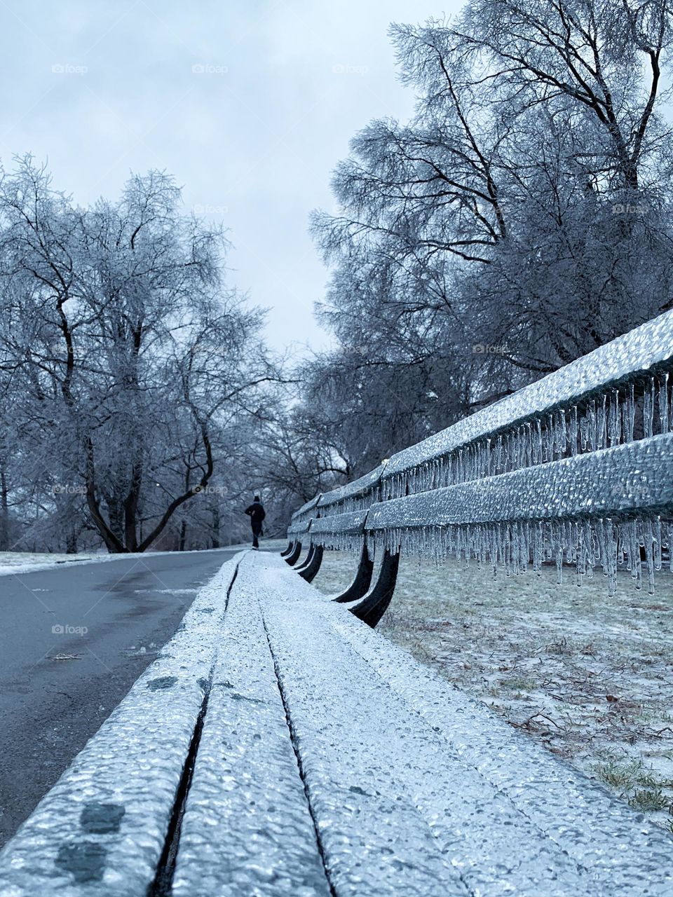 A wooden green bench covers a layer of ice and icicles after freezing rain in winter. 