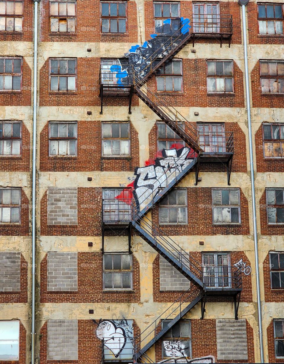 A fire escape zigzags down the side of an old building and has become a platform for graffiti artists