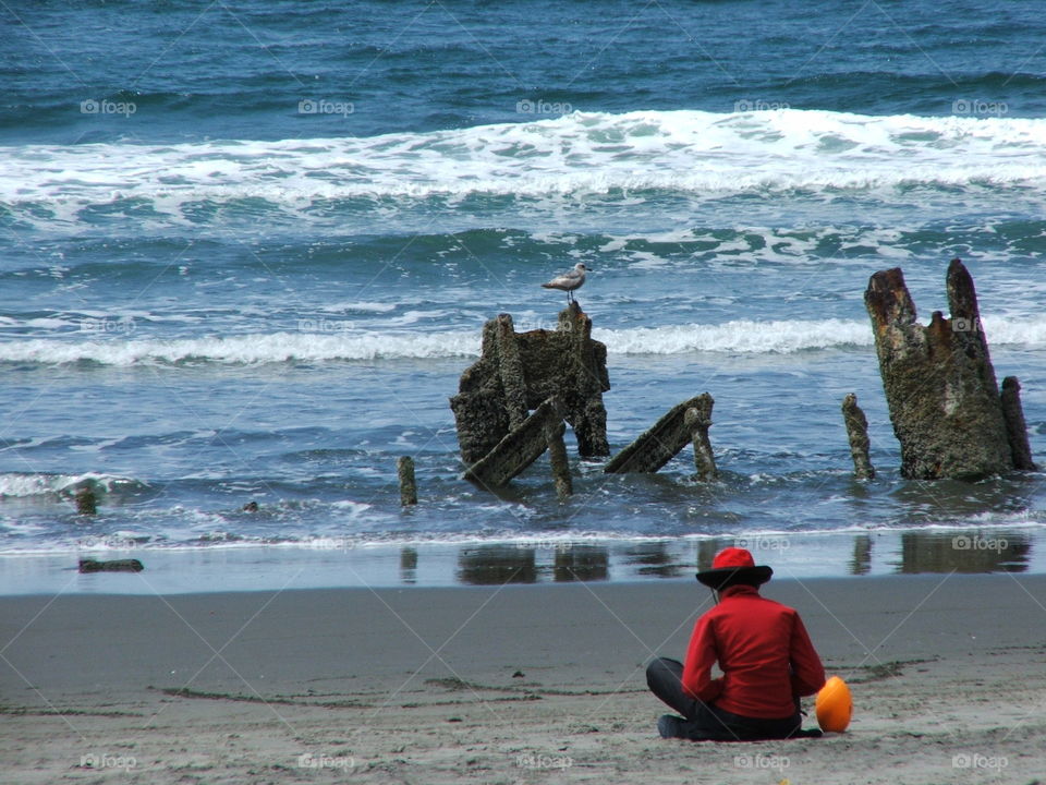 The beach lounger . Woman in red enjoying the beach next to a hollowed out shipwreck near Astoria, Oregon