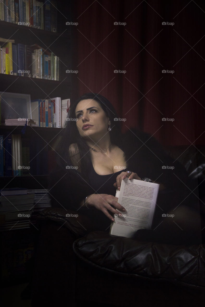 A portrait of a beautiful woman thinking of something while reading a book in a little library setting. she really looks lost in thought.