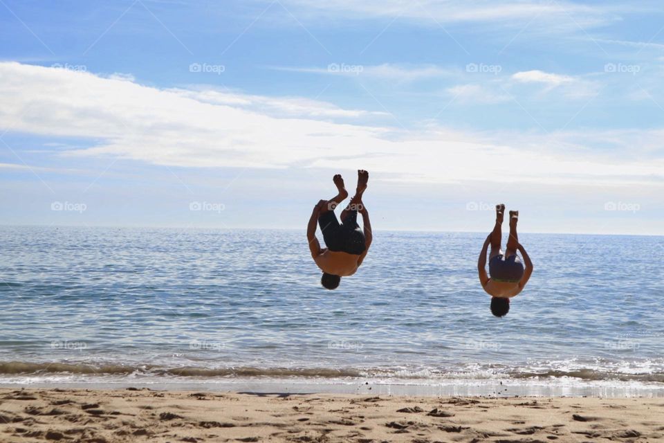 Two kids practicing their gymnastics skills with perfect timing flip on the beach