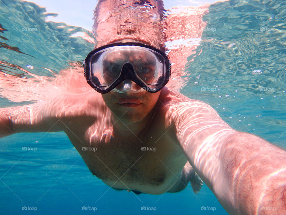 Man diving, male underwater smiling,swimming and relaxing in big blue sea with his camera