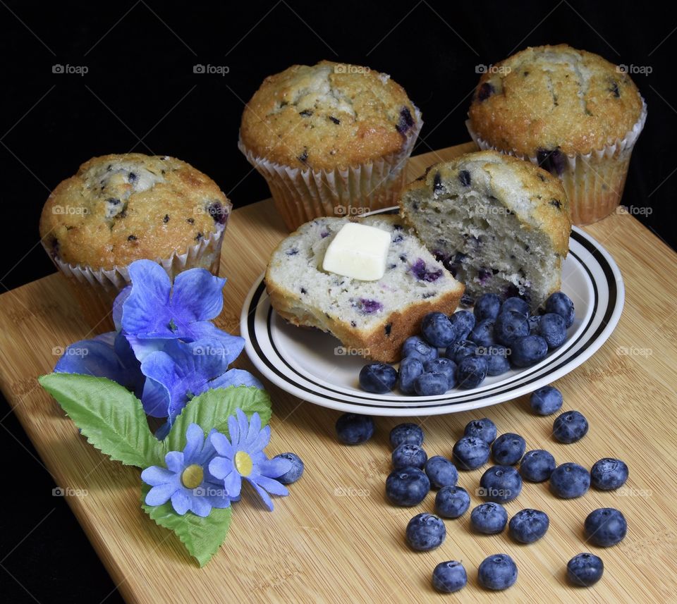 Blueberries and blueberry muffins on a table with blue flowers 