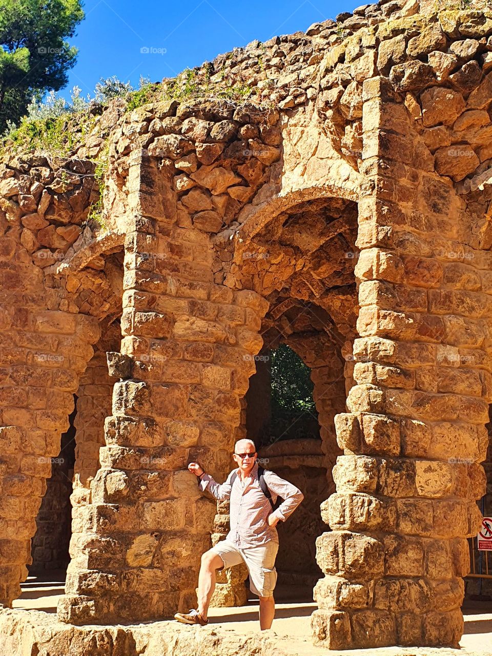 A man resting along one of Gaudi's creations in Park Güell, contemplating the view