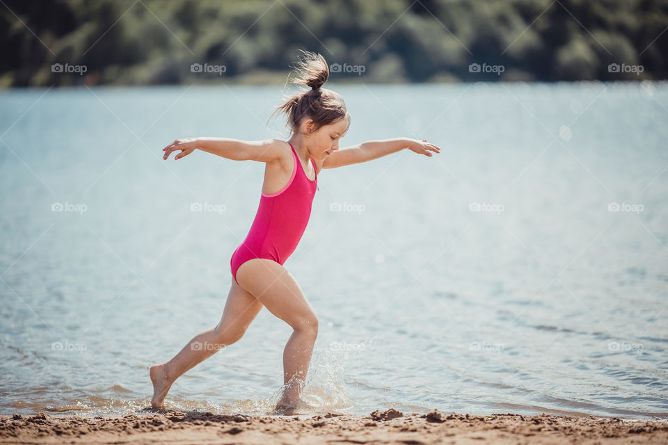 Little girl on lake coast at sunny evening. 