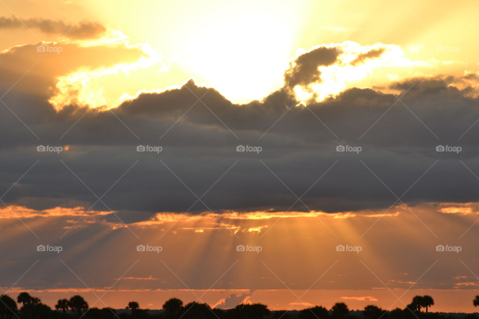 Orange sun rays streaming down from a dark cloud with the golden sunlight above at sunset