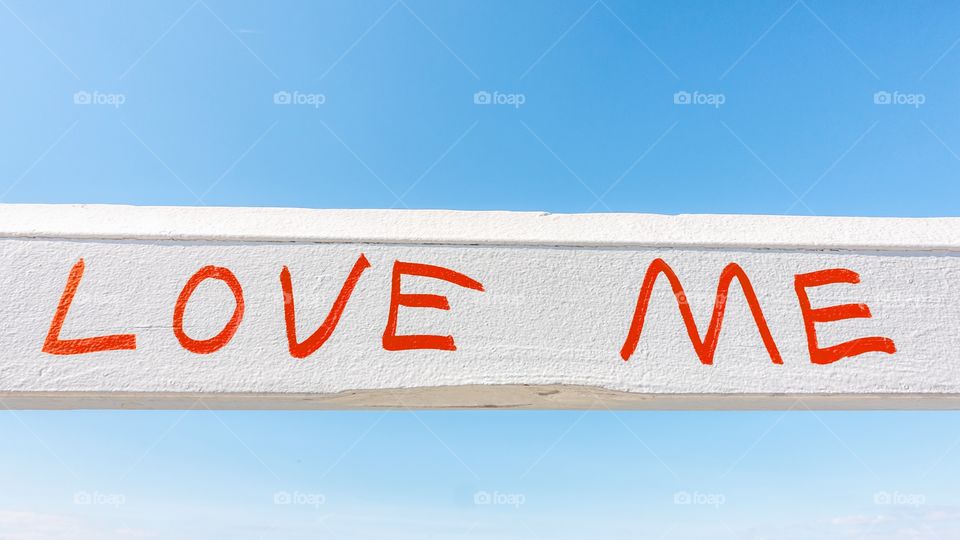 The wods Love me written in red on a white woiden fence against a blue sky