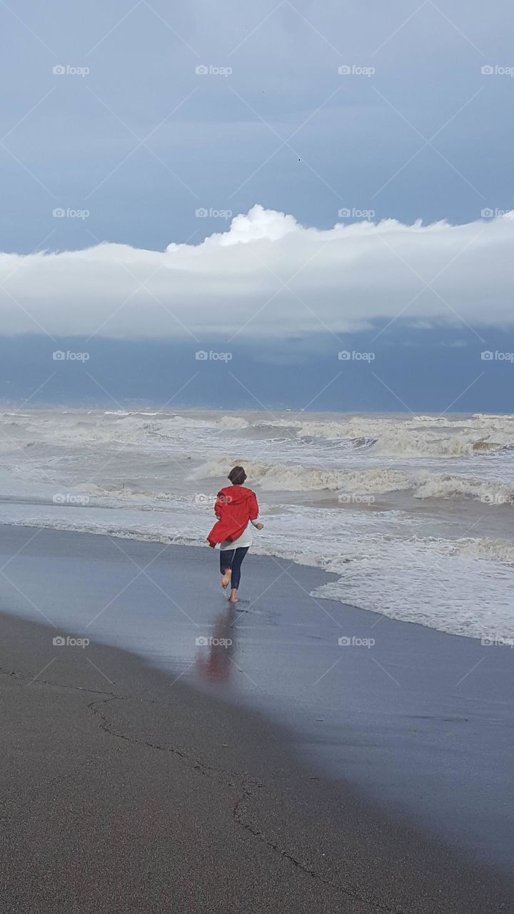 Storm on the sea, waves and wind. A girl in a red raincoat runs along the seashore.