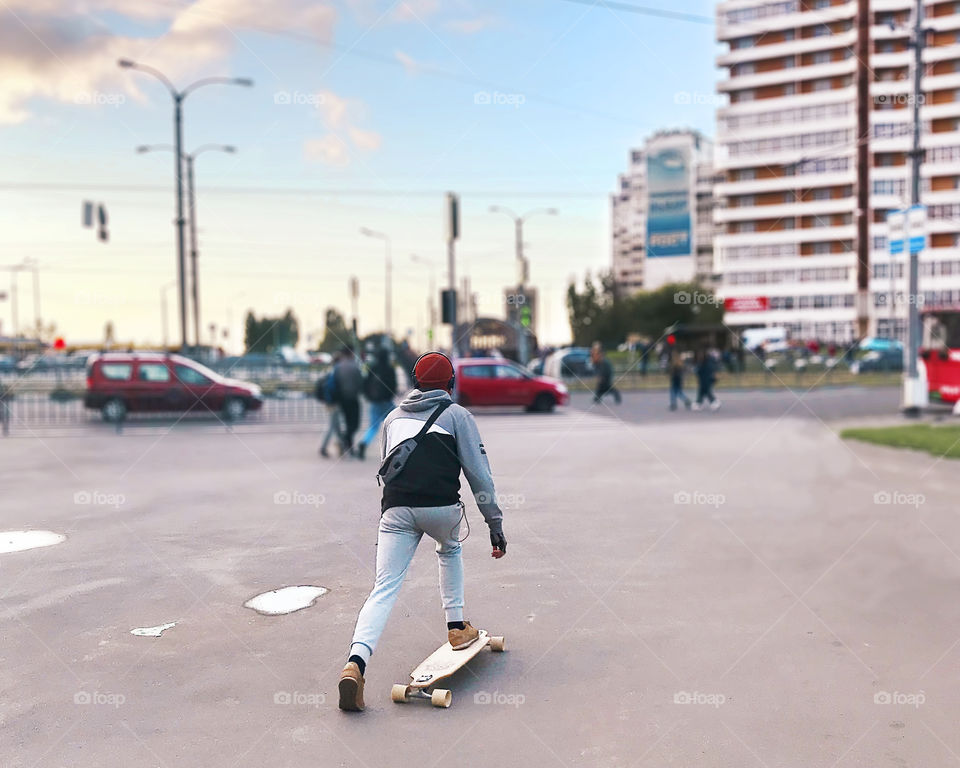 Young man wearing a sporty clothes skateboarding in the city with headphones 