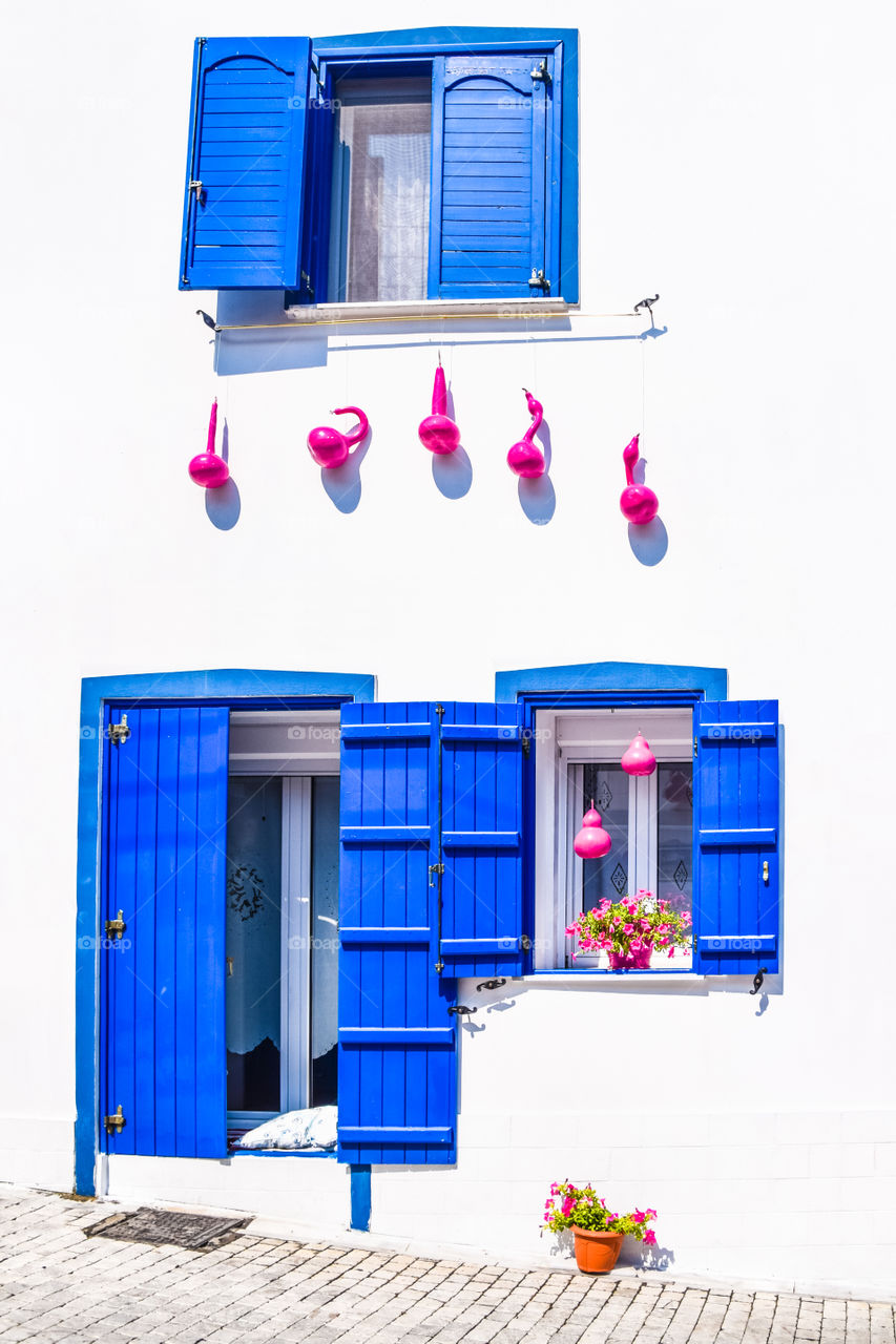 Greek Traditional House With Blue Windows , White Wall, Flowers And Pink Decorative Pumpkins