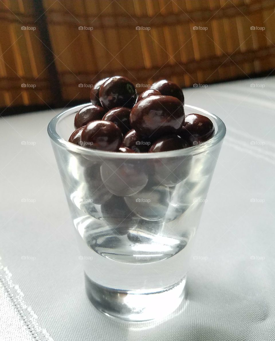 shot glass of chocolate candies, close-up, white foreground, bamboo backdrop