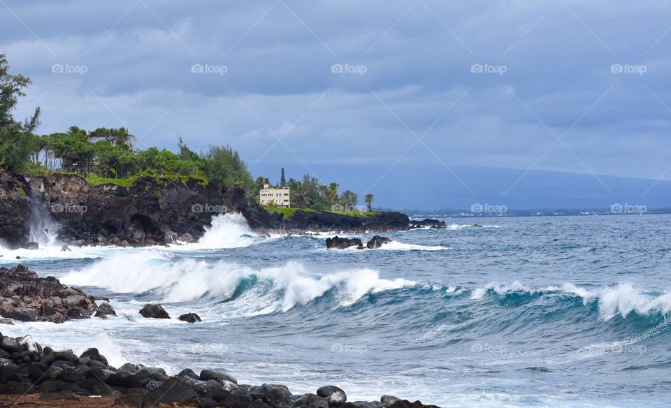 Big waves making their way to the lava shores with Mauna Loa volcano rising out of the ocean in the distance