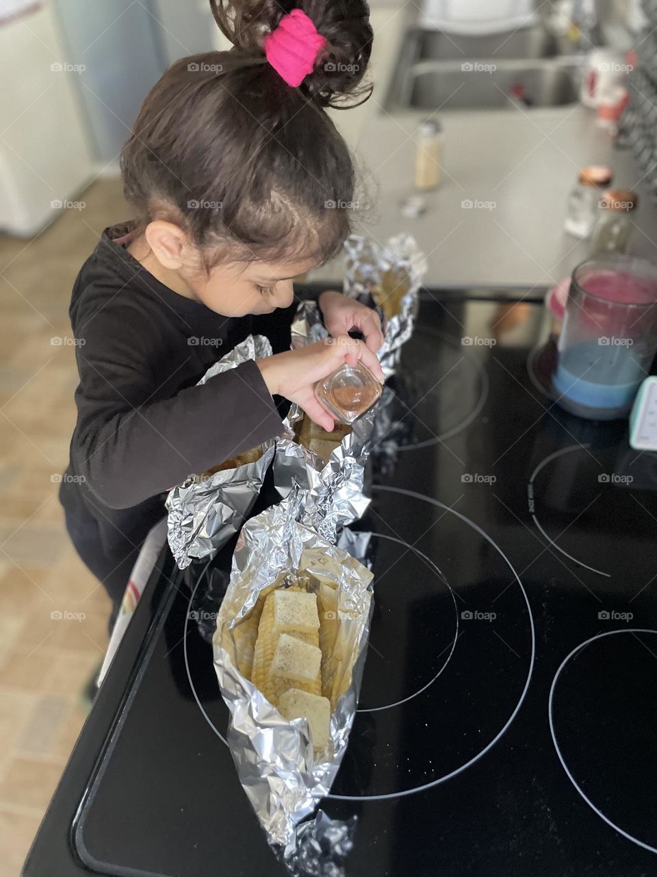 Toddler girl helps mommy cook, making corn on the grill, grilling out in the summertime, delicious corn with butter and seasoning, toddler girl helps mother 