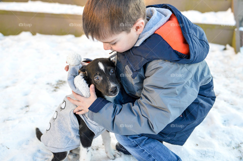 Child petting his pet puppy outdoors in the snow 