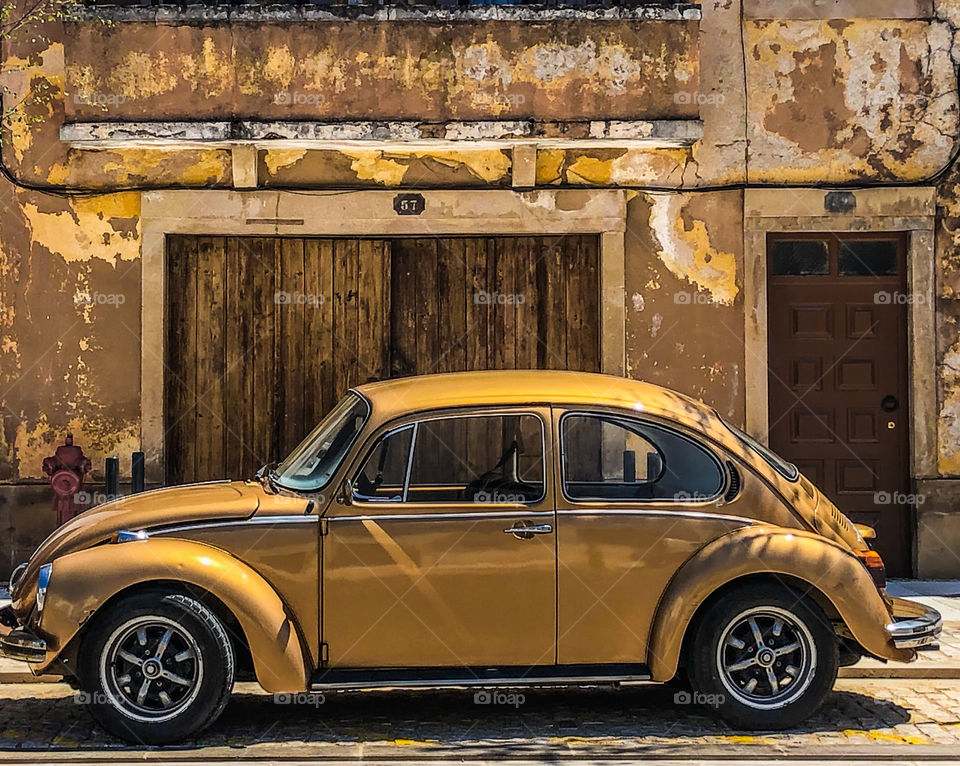 Gold Volkswagen Beetle parked on the street in front of a similar coloured background 