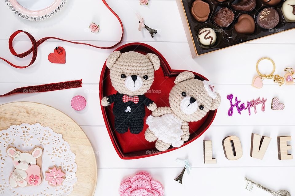 Happy anniversary present : bride and groom teddy bear crochet dolls or amigurumi, handmade bunny cookies and a box of chocolate on the white wooden board. Romantic Valentines gift. Selective focus.